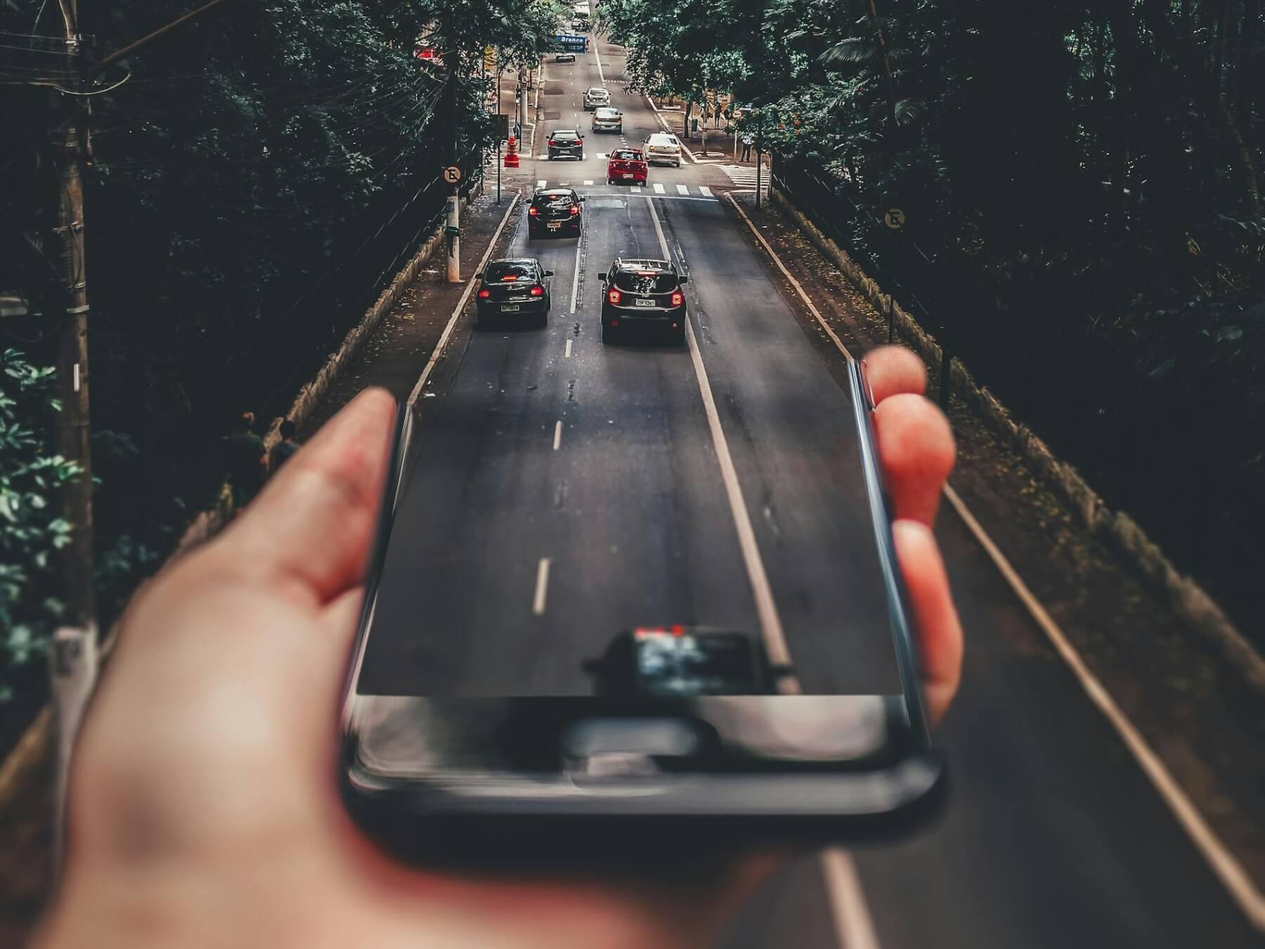 Digitally manipulated image of cars on road coming out of smartphone