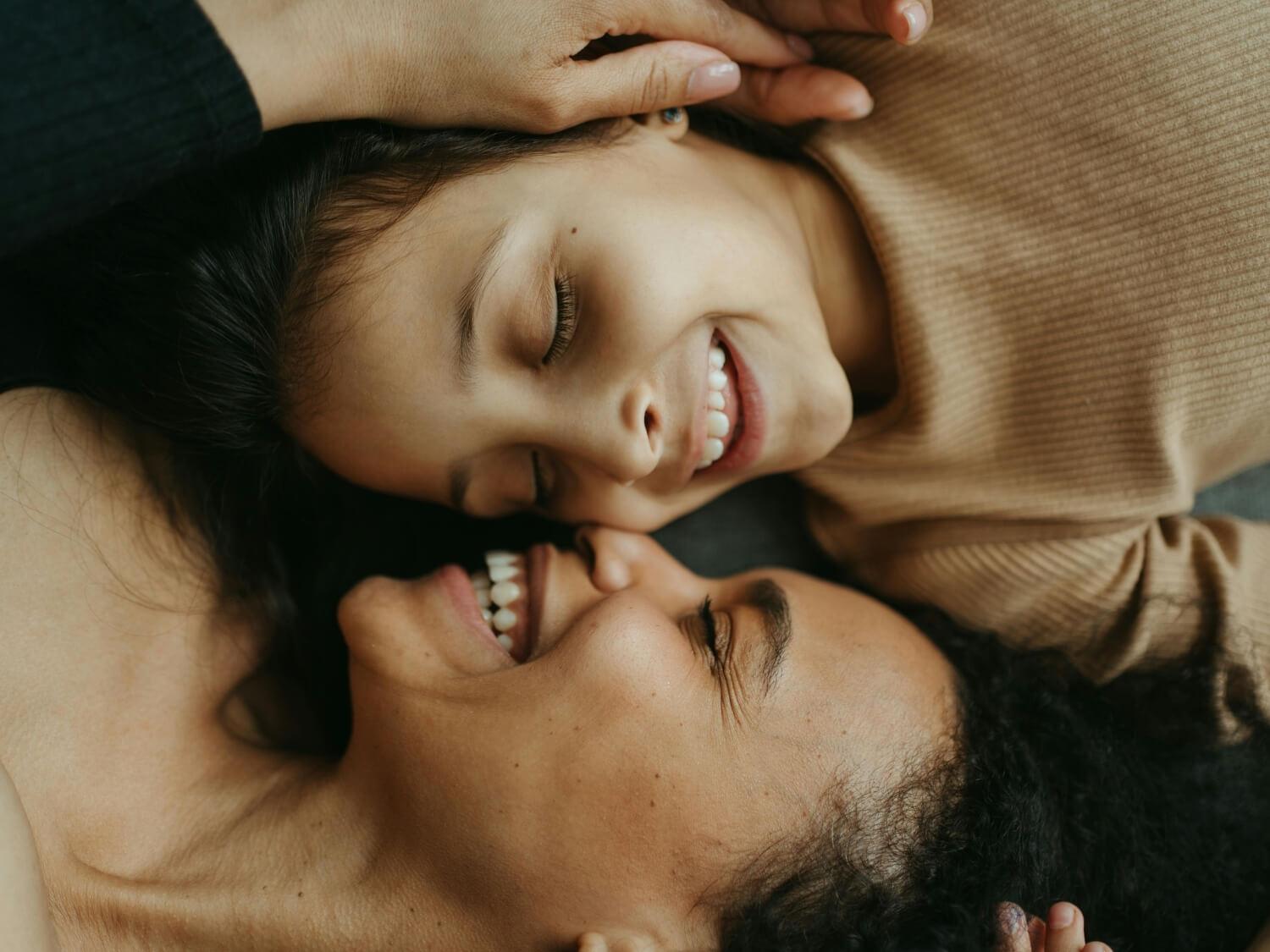 A mother and child lying side by side and smiling.