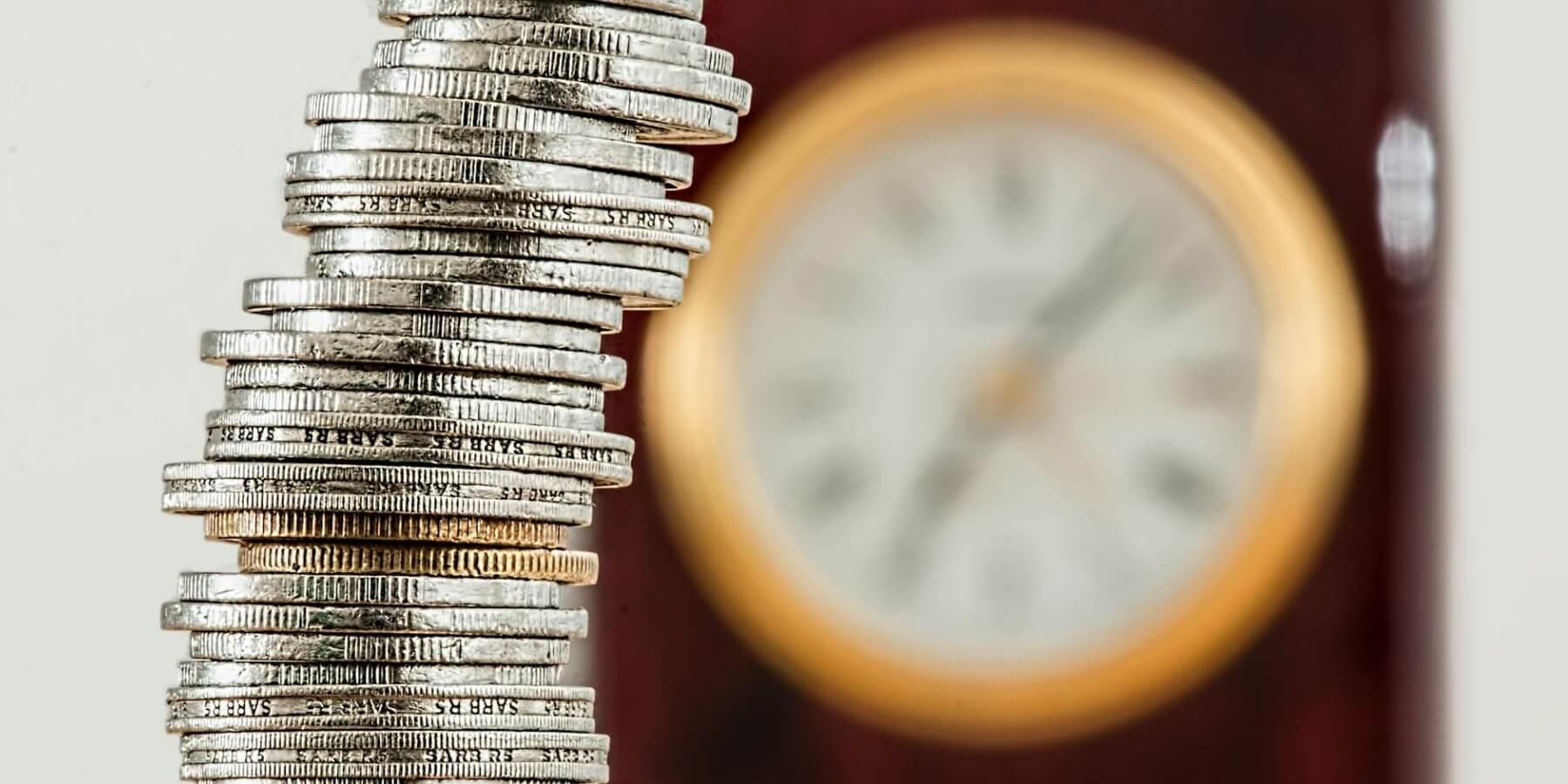 A stack of coins with a clock in the background illustrating the cost risks associated with leaving an archive unmanaged over time.