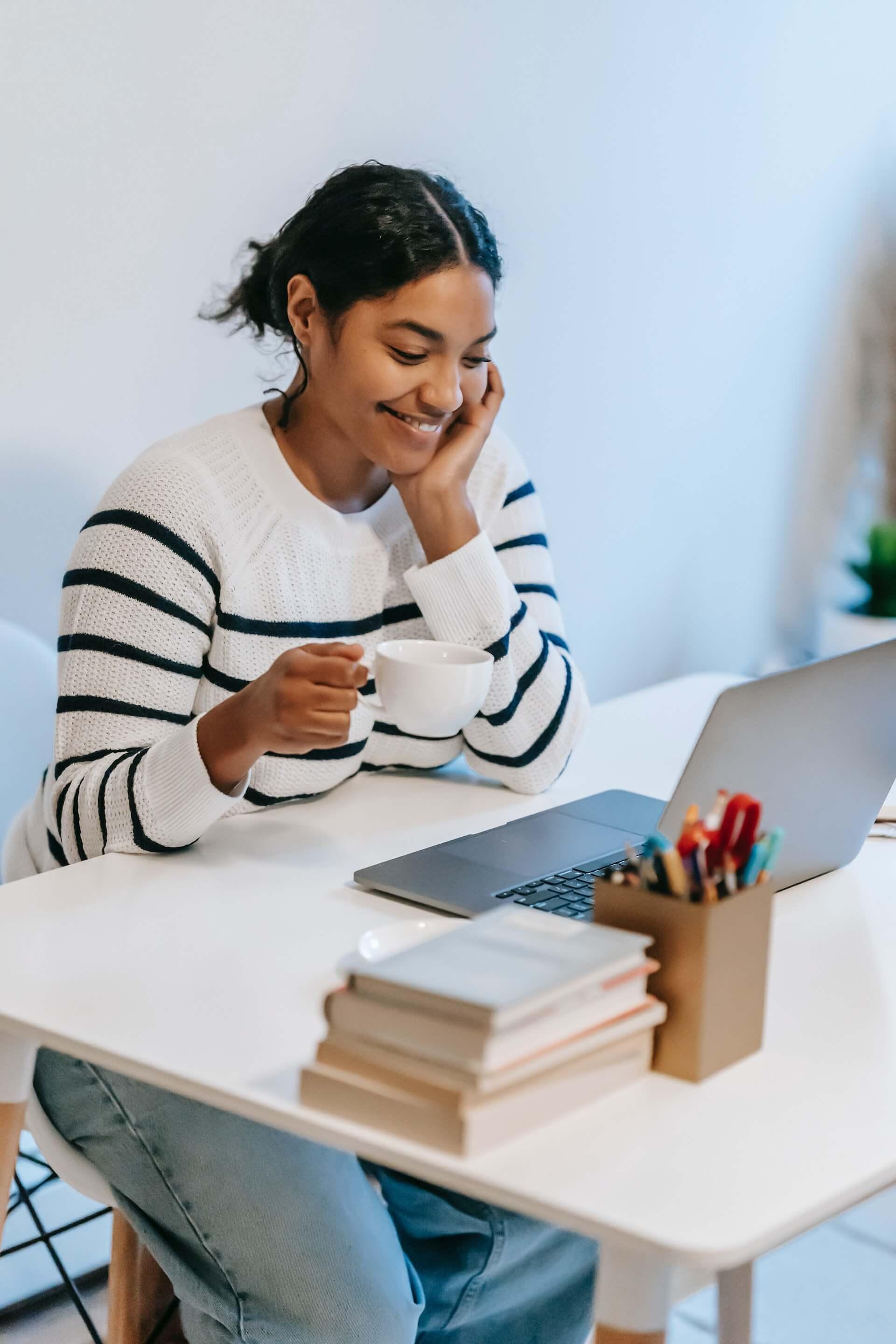 Smiling young ethnic woman working distantly on laptop and talking on smartphone.