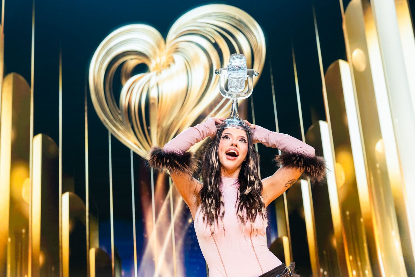A Eurovision Song Contest winner holding the glass microphone trophy above their head on stage