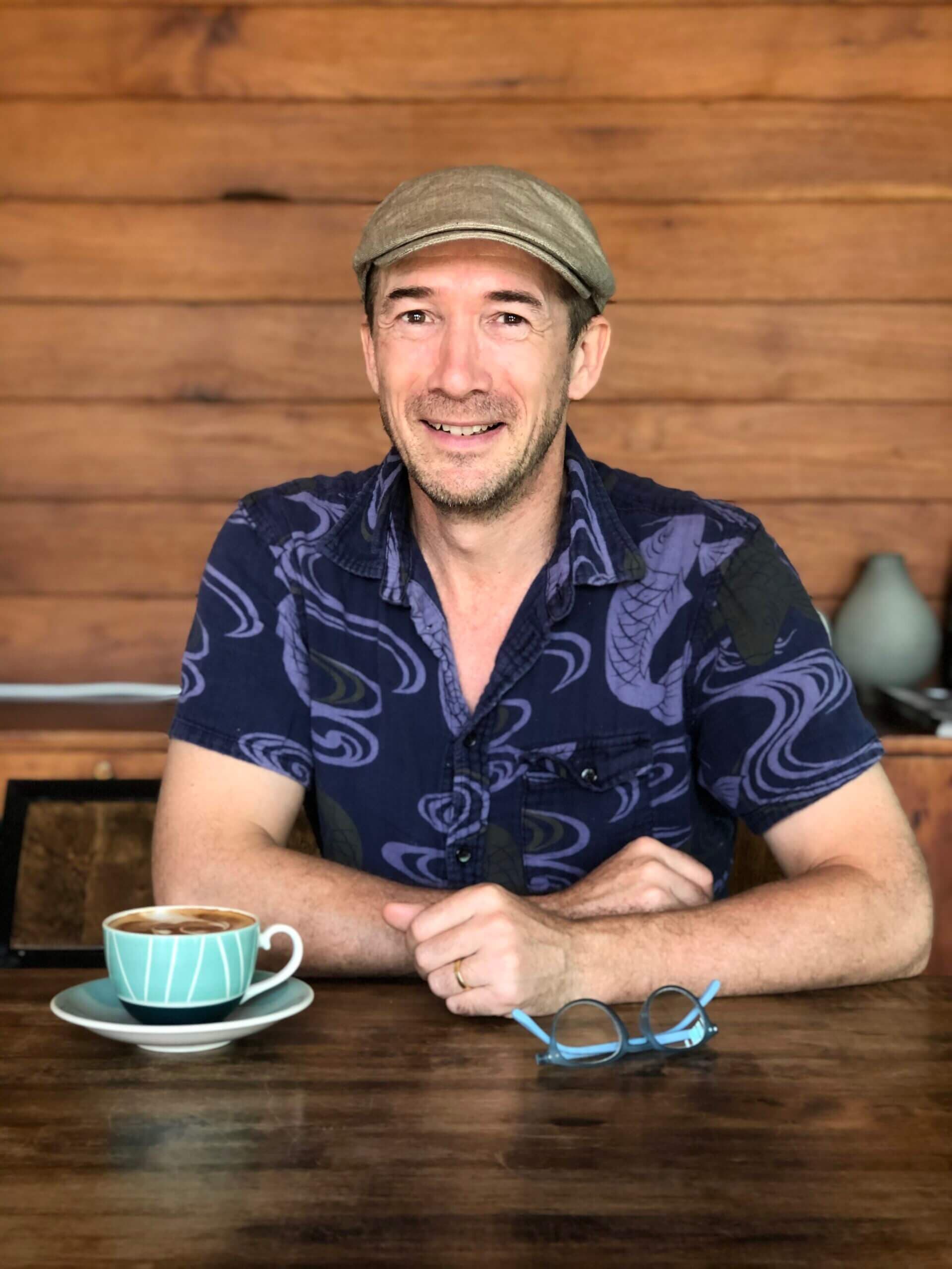 Yvan Cohen sitting at a wooden table with a cup of coffee.