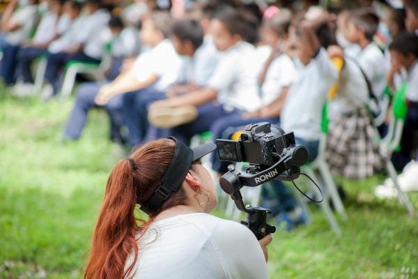 Photographe scolaire filmant une assemblée d'élèves lors d'un événement scolaire en plein air.