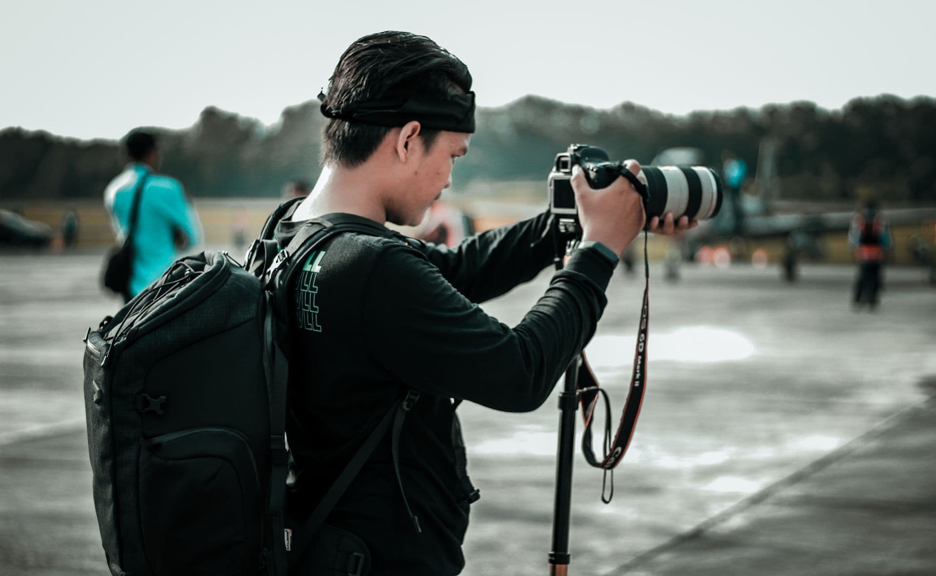 A photographer silhouetted against a clouded sky, working from a tripod on a rocky summit