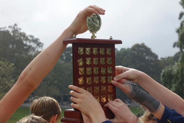 Élèves levant un trophée sportif scolaire ensemble lors d'un événement sportif en plein air.