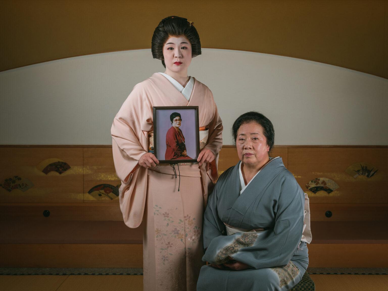 Mai Watanabe (L) poses holding her grandma picture as her mom Michiyo sit beside for a portrait picture inside a restaurant called Mangero on April 24, 2022 in Aizuwakamatsu, Japan. Mai Watanabe is the 3rd generation of Geisha from her family’s geisha house called “Hana no Ya”. Her grandmother founded the house in 1954 in Higashiyama Onsen, Aizuwakamatsu. Photo by Nicolas Datiche
