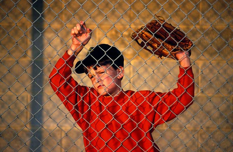 Young baseball player, glove in hand, looks dejected on the sidelines. See more of John Greim’s work here.